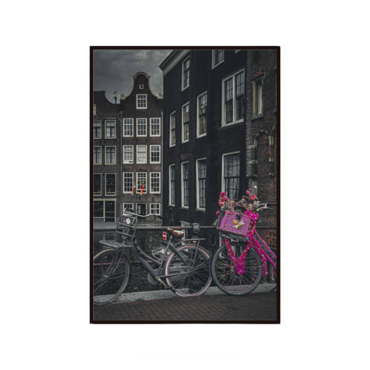 Pink bicycle with floral decorations in front of traditional Dutch houses.