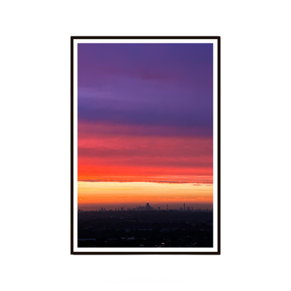 Framed artwork of a city skyline at sunset with a gradient sky from purple to orange.